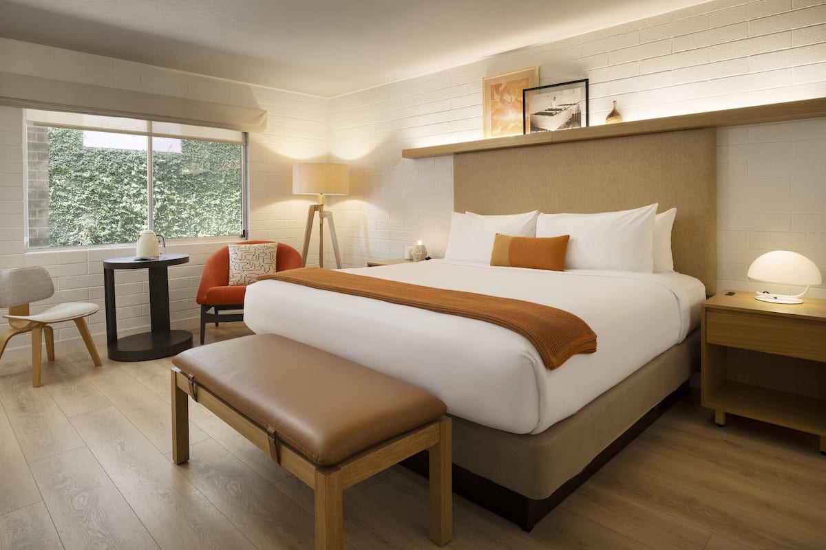 A hotel room with a large bed, a bench, a desk, and a chair.