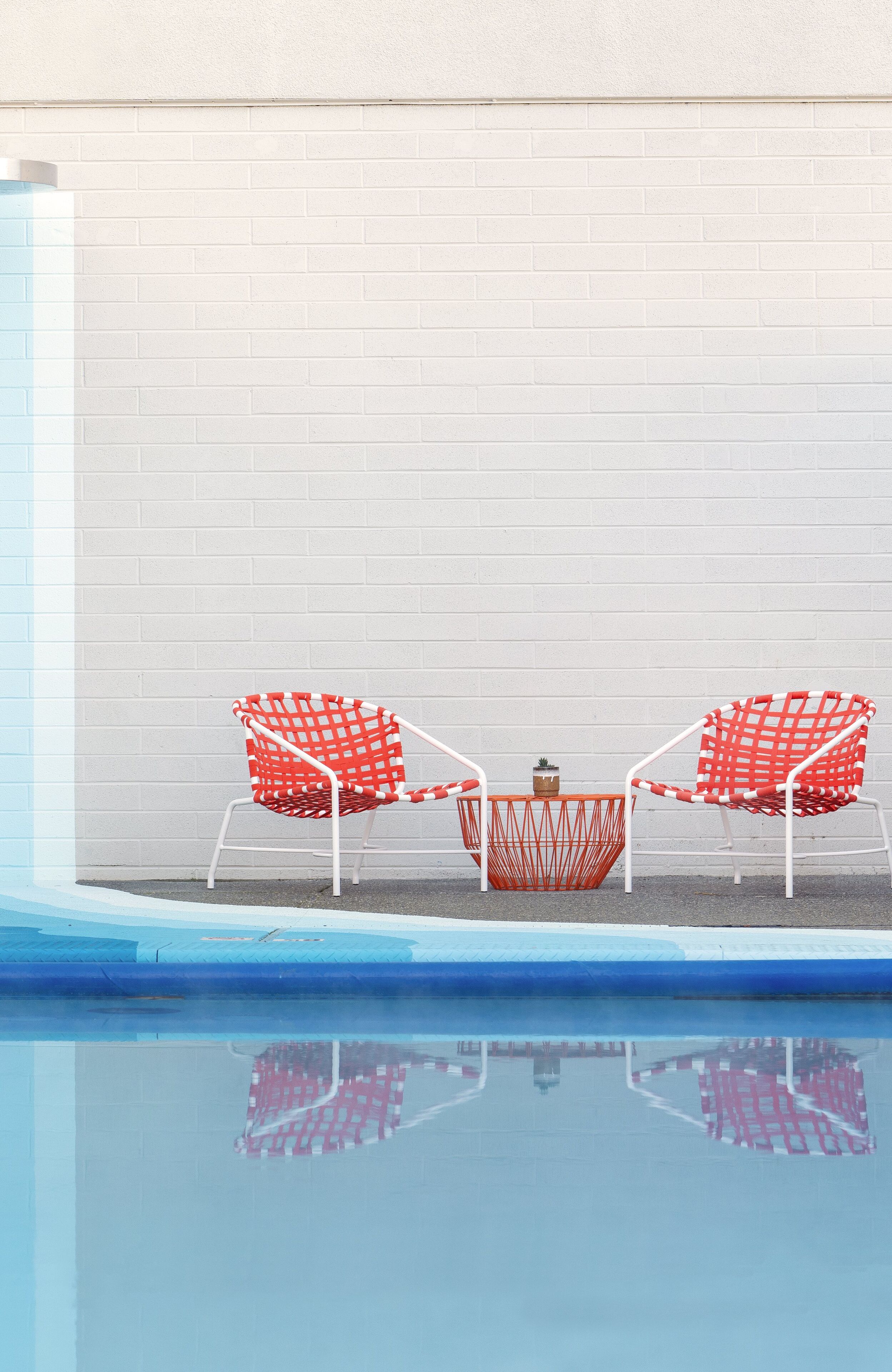 A poolside area with two red and white checkered chairs and a small table.