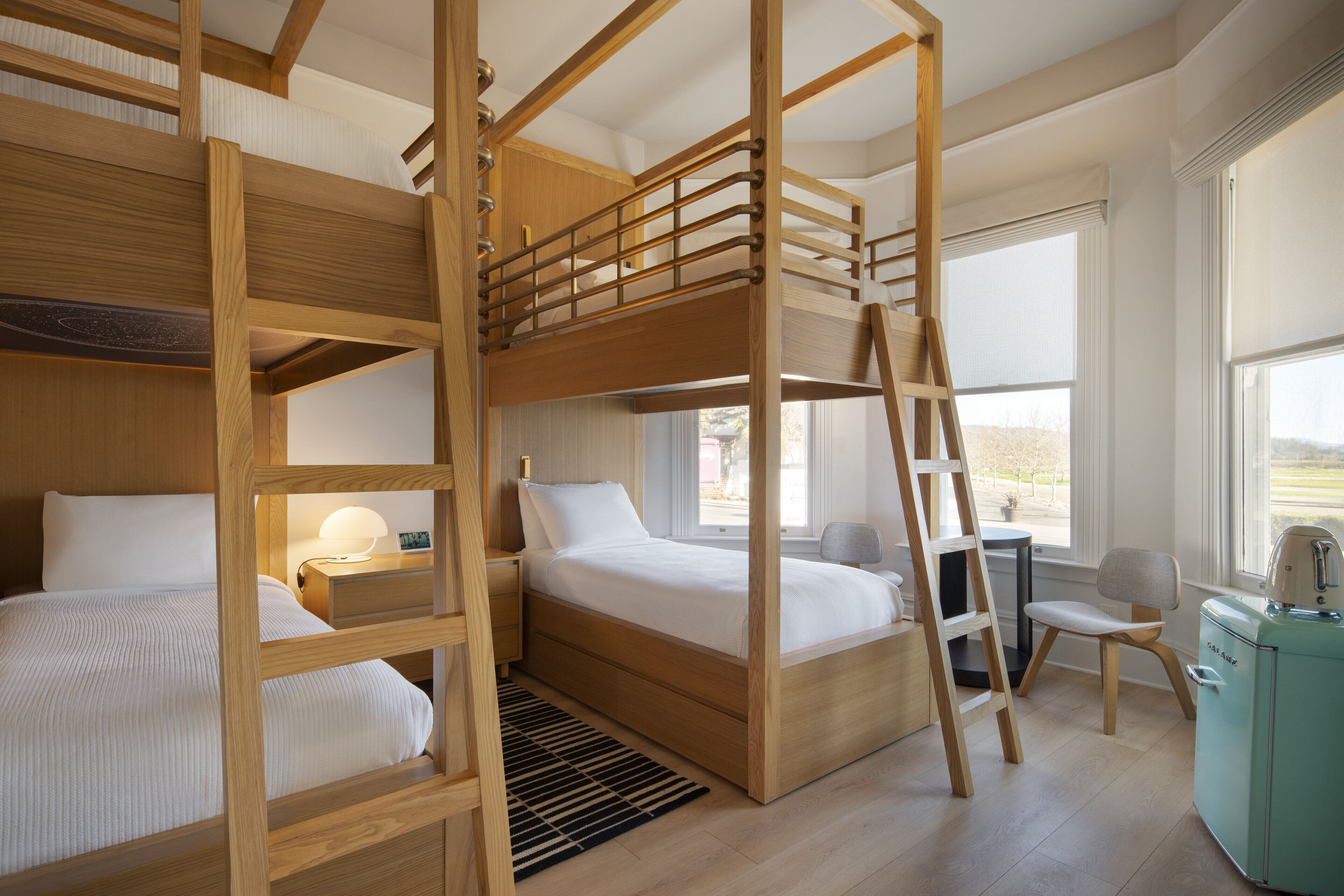 Une chambre avec un lit superposé doté de barrières en bois, un bureau, une chaise et un coin cuisine.