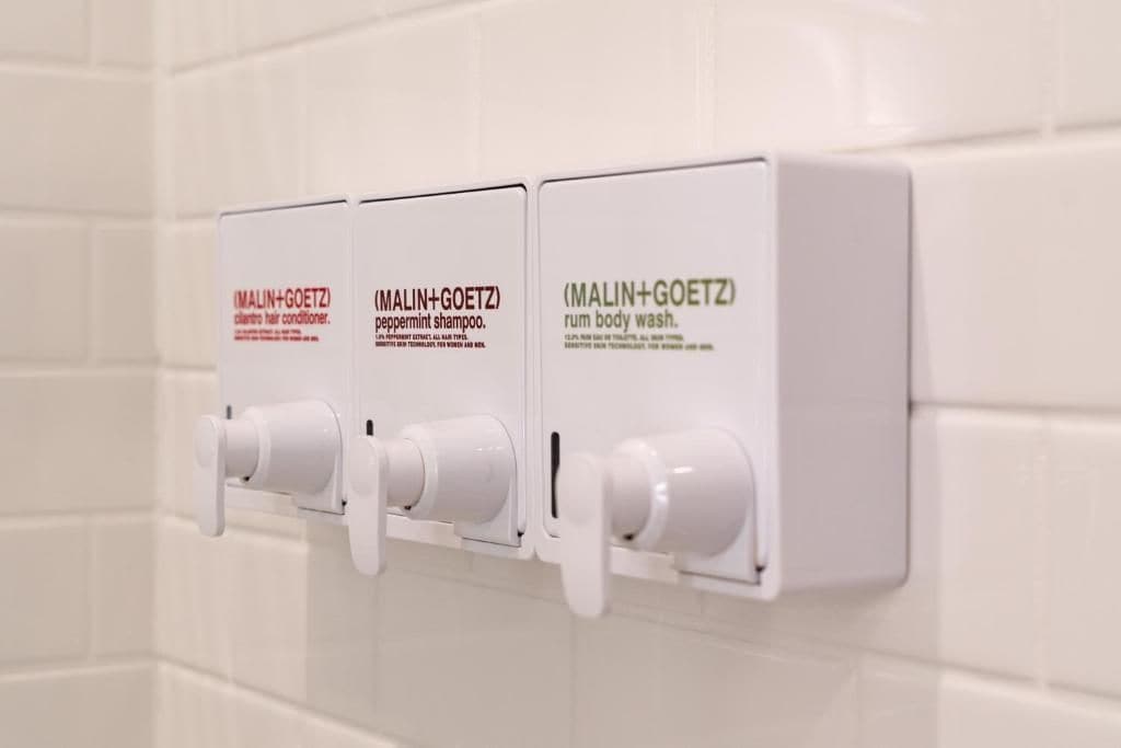 A set of three white dispensers on a wall, each labeled with different product names.