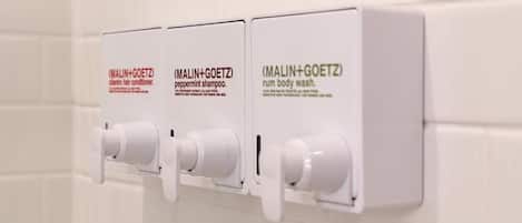 A set of three white dispensers on a wall, each labeled with different product names.