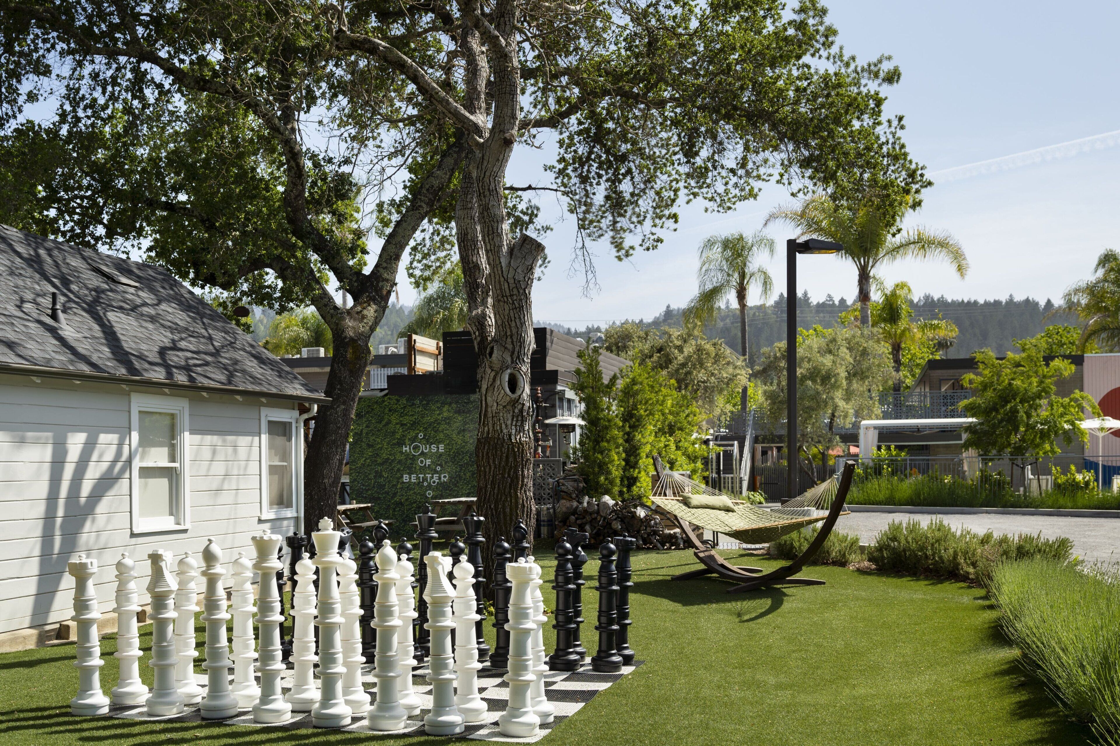 A chessboard with oversized pieces set up in a garden area, a hammock, and a house with a sign that reads "House of Better."
