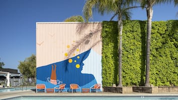 Relax by the pool surrounded by lush greenery and a vibrant mural depicting a serene sailboat scene.