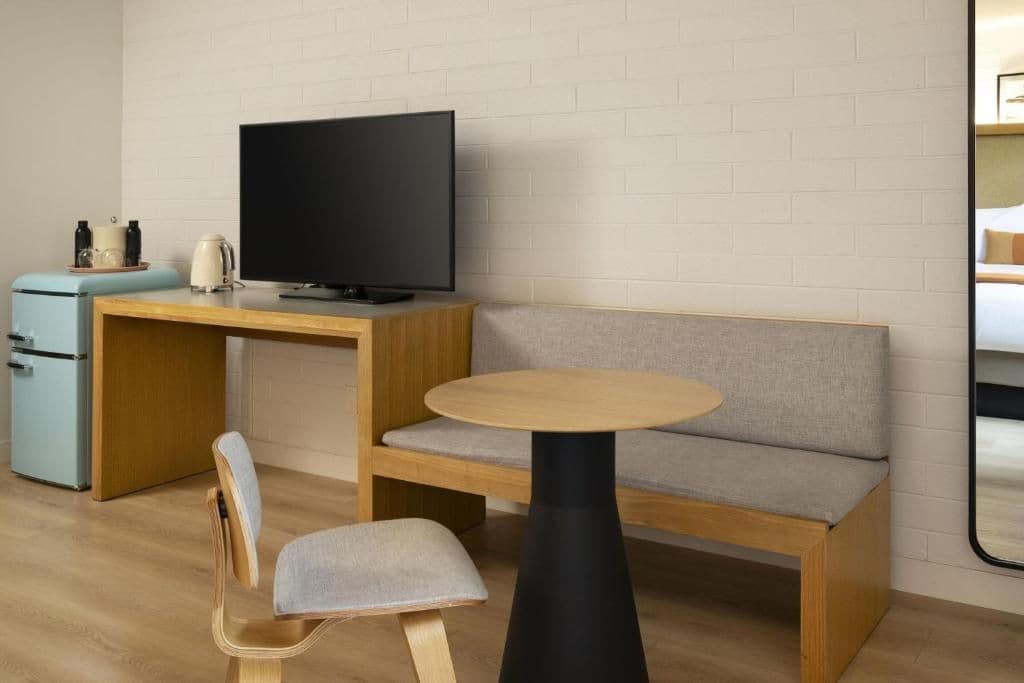 Une pièce compacte comprenant un bureau en bois, une télévision, une petite kitchenette, une table ronde et un canapé.