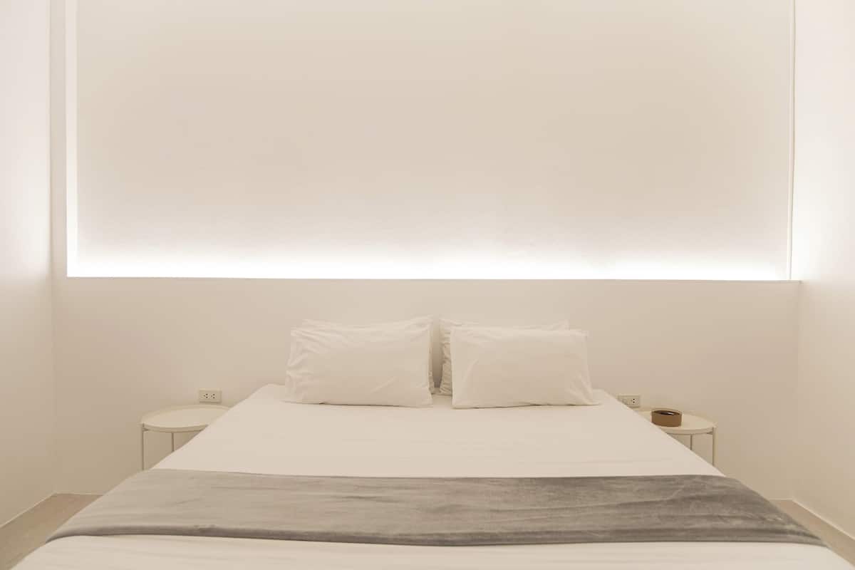 A minimalist hotel room with a large bed, two bedside tables, and a wall-mounted light fixture.