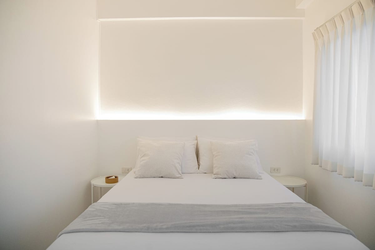 A minimalist hotel room with a bed, bedside tables, and a wall-mounted light fixture.