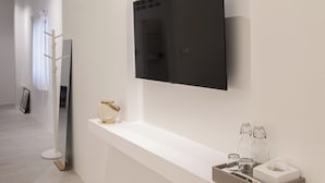A modern hotel room with a large flat-screen TV mounted on the wall, a minimalist console table with a tissue box and glasses, and a long hallway with a light-colored floor and a white wall. - HAO HOSTEL PHUKET (Phuket)
