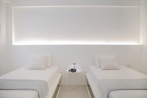 A minimalist hotel room with two beds, a small table, and a wall-mounted light fixture. - HAO HOSTEL PHUKET (Phuket)