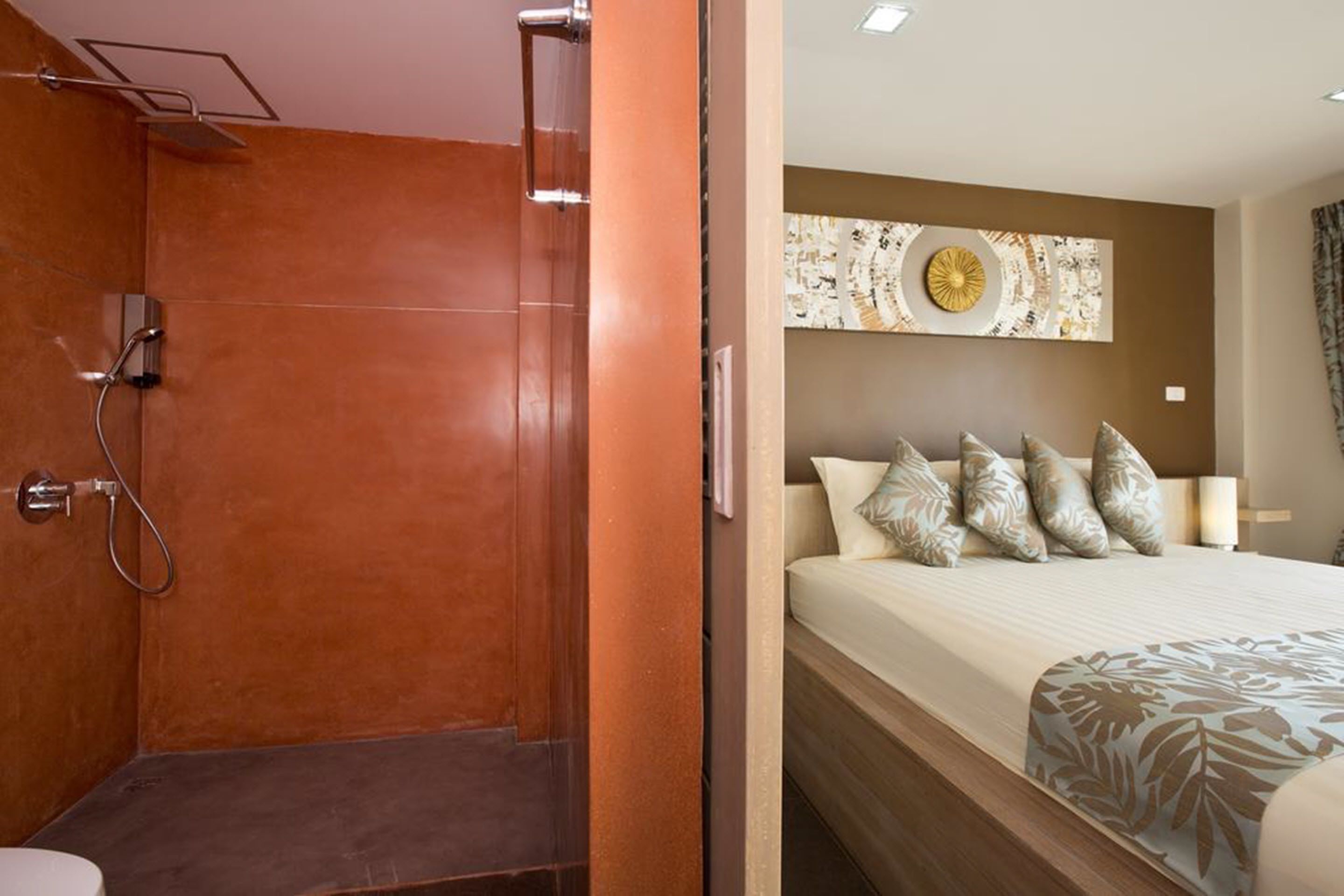 Ein Hotelzimmer mit Dusche, einem Bett mit gemusterten Laken und einem dekorativen Wandbild.