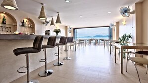 Zona de bar moderna con taburetes altos, una barra con botellas y vistas al mar.