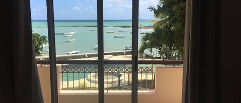 Uma varanda com vista para o mar, barcos e uma palmeira.