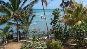 Tropisch strand met palmbomen en boten in het water.