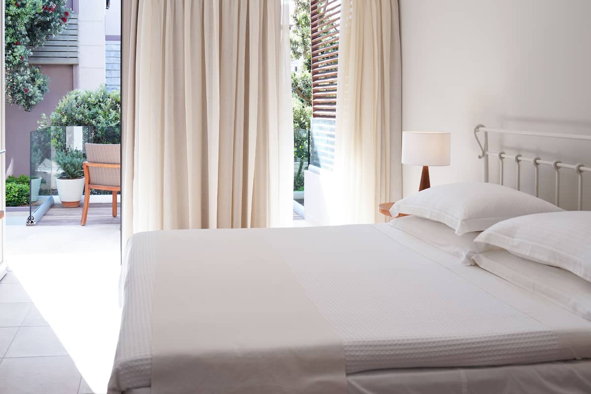 A hotel room with a large bed, a bedside table with a lamp, and a view of the outdoor balcony.