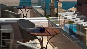 Un balcón con mobiliario de mimbre, una mesa y baranda de vidrio con vista al mar.