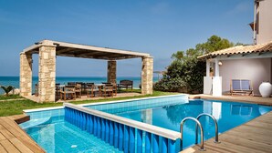Zona de piscina con un pérgola, mobiliario exterior y vista al mar.