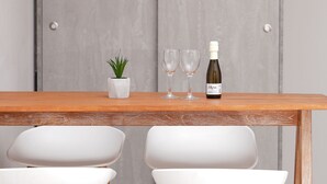 Una mesa de comedor con dos sillas blancas, una pequeña planta en maceta, dos copas de vino y una botella.
