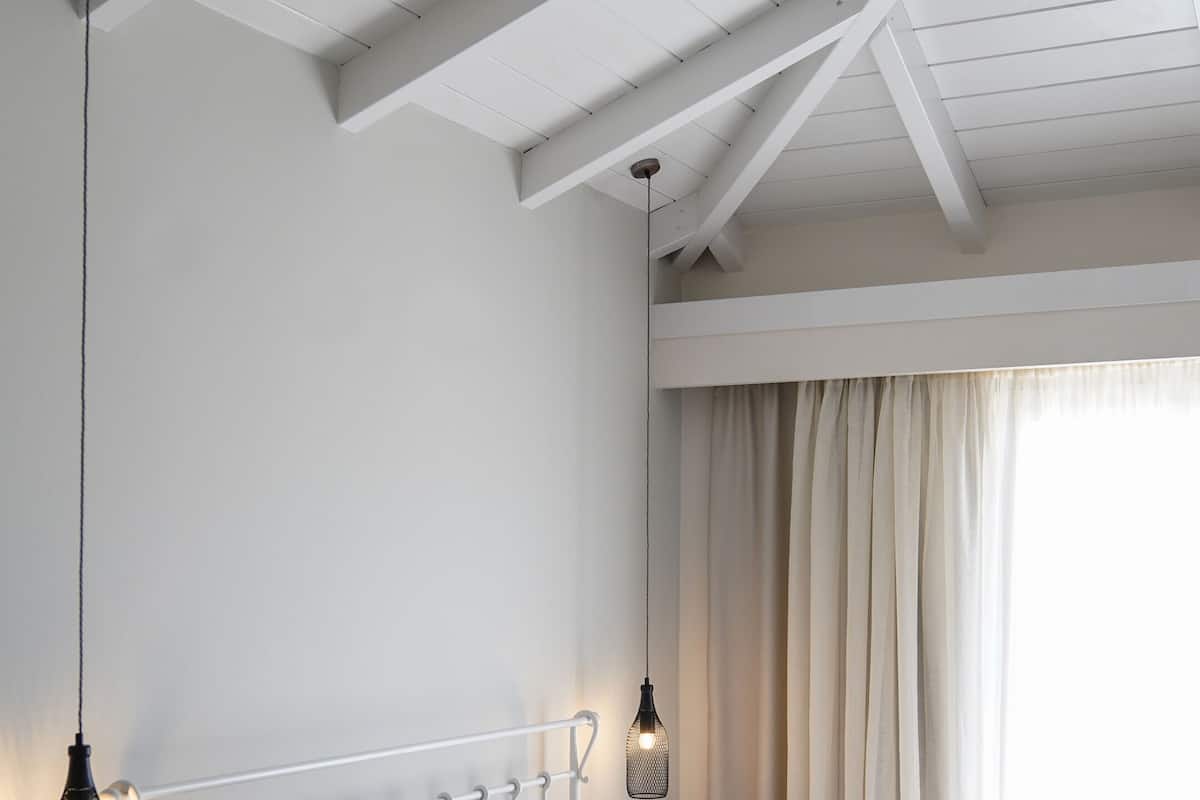 A bedroom with a bed, a nightstand, a hanging light fixture, and a window with curtains.