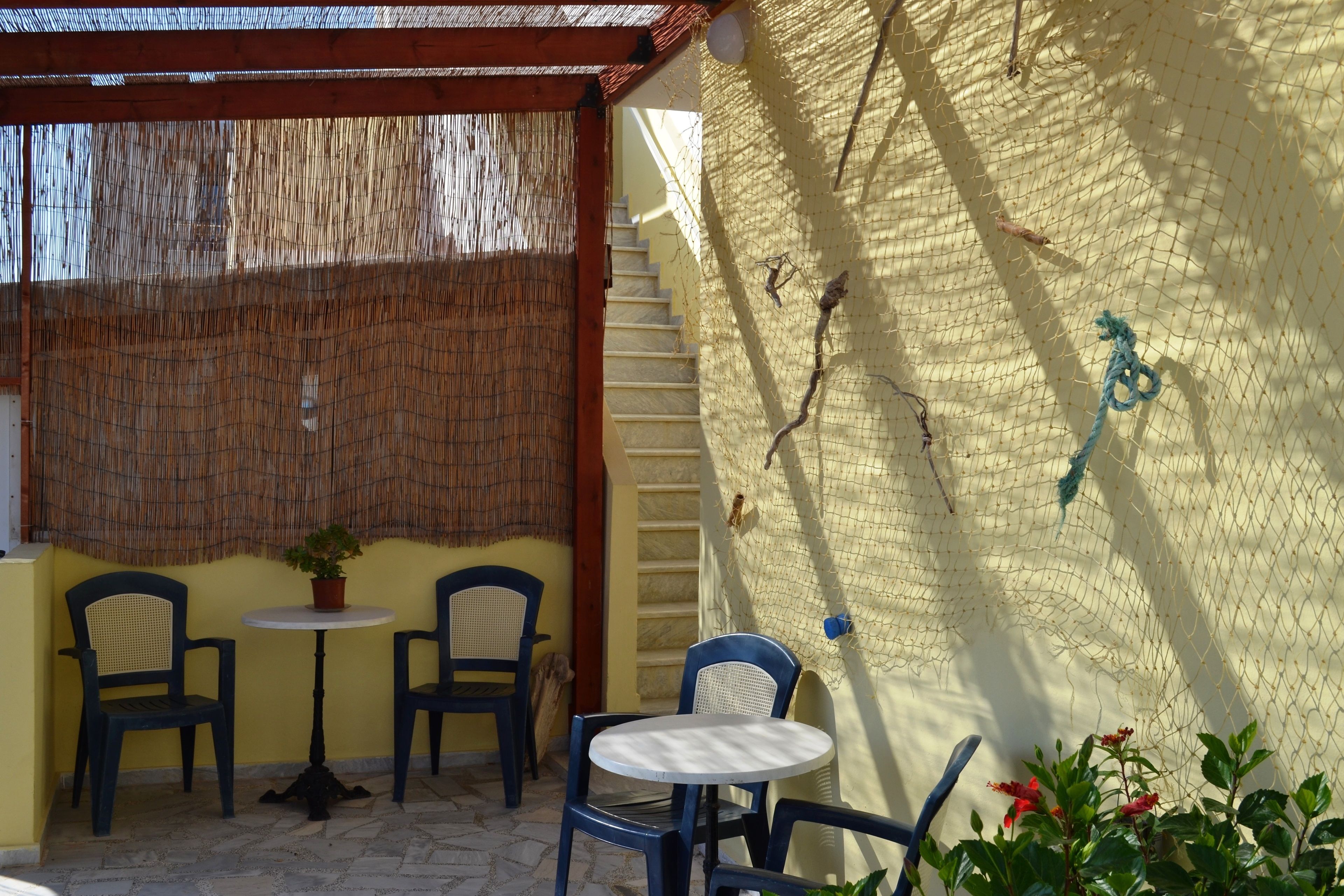Pátio externo com duas cadeiras, uma mesa, escadas e um muro com tela.