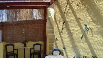 Pátio externo com duas cadeiras, uma mesa, escadas e um muro com tela.