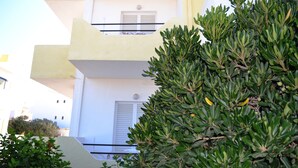 A building with balconies and a green bush in the foreground. - Yiannis Apartments (Kos)