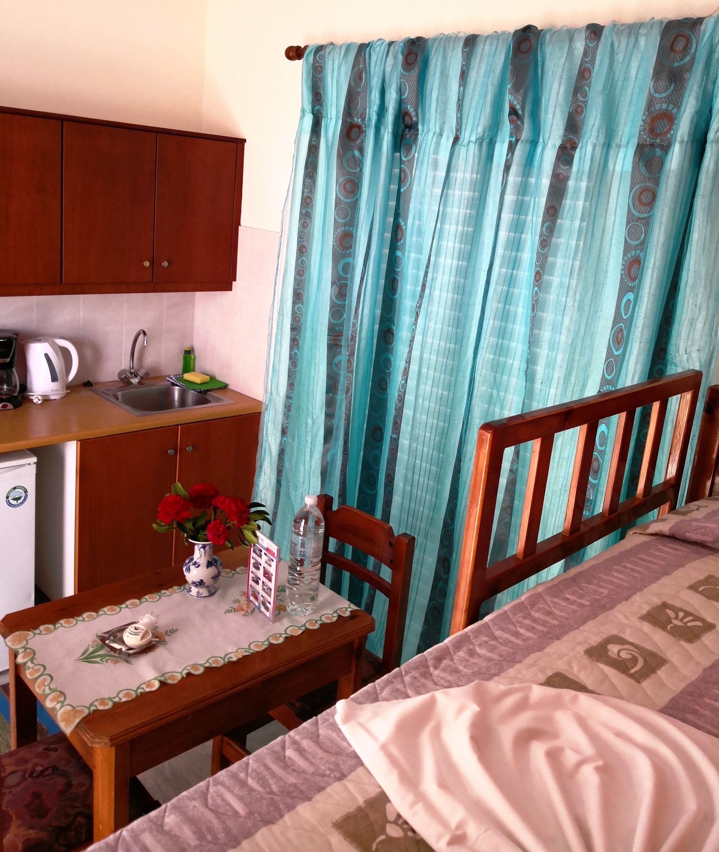 A compact room with a bed, a small table with a vase of flowers, a water bottle, and a coffee maker.