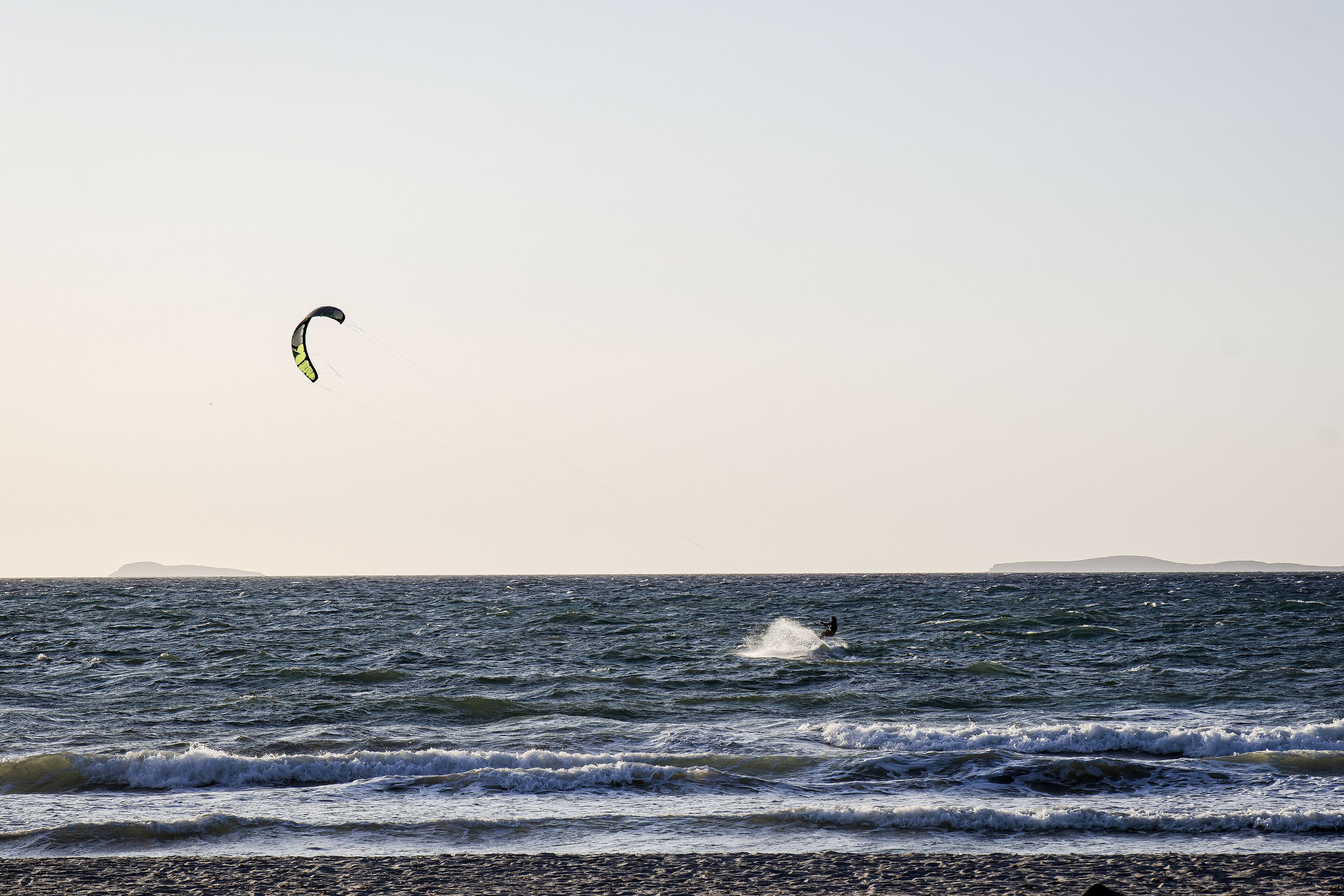 Una playa con olas y una cometa en el cielo.