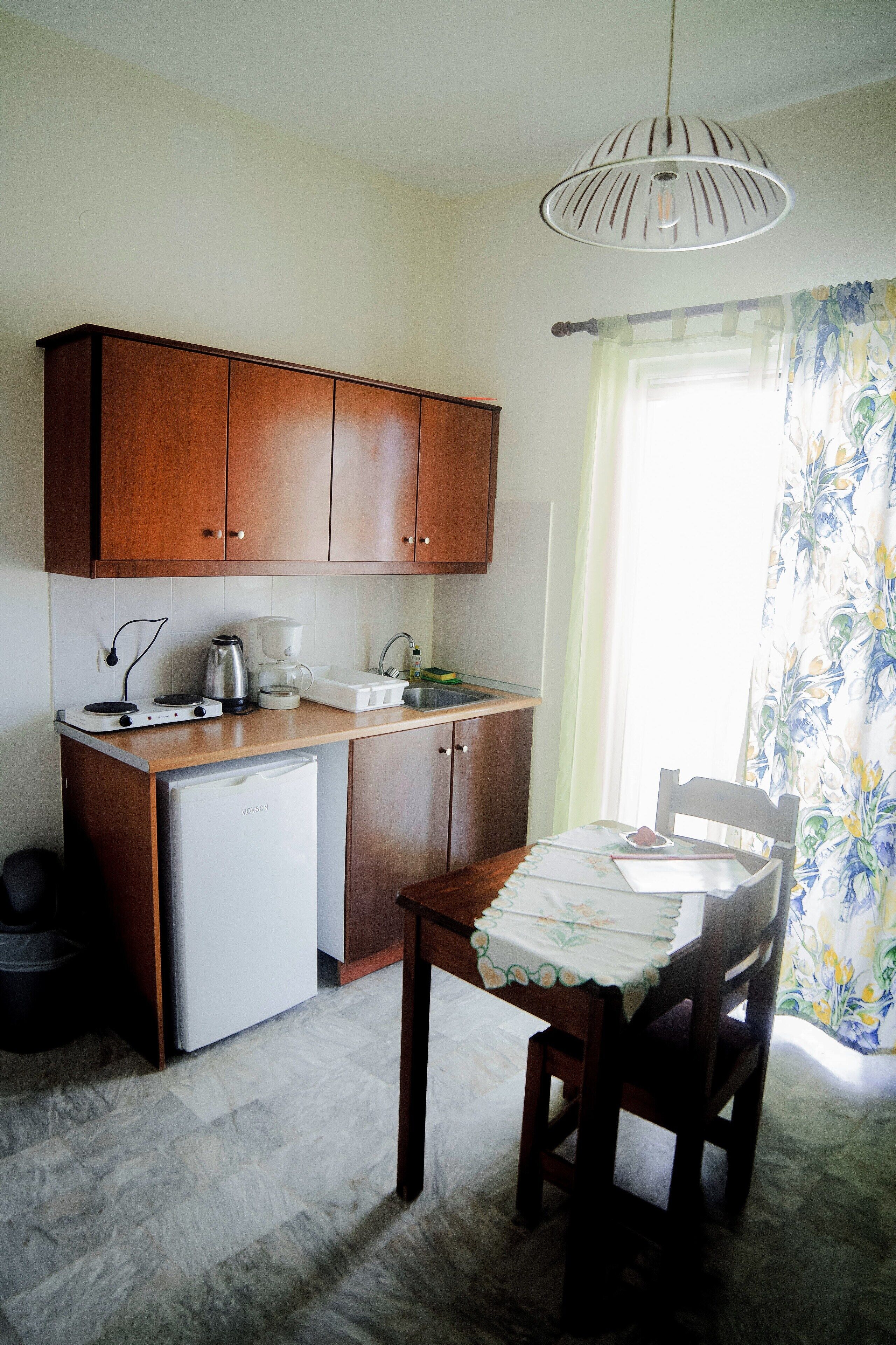 Una cocina compacta con armarios de madera, lavavajillas integrado, cafetera y una mesa de comedor con mantel floreado.