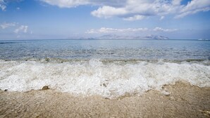 A beach with waves gently lapping at the shore, a clear sky, and distant mountains. - Yiannis Apartments (Kos)