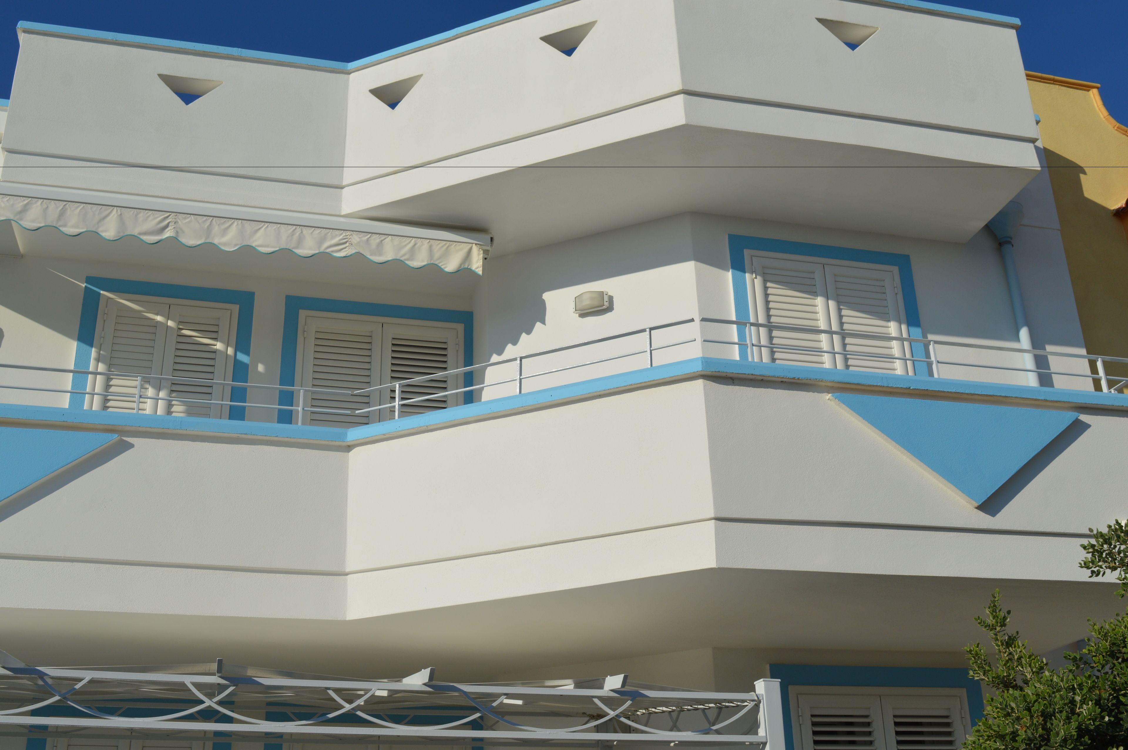 A multi-story building with a white facade, blue trim, and a balcony with railings.