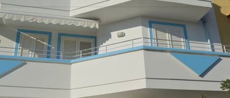 A multi-story building with a white facade, blue trim, and a balcony with railings.