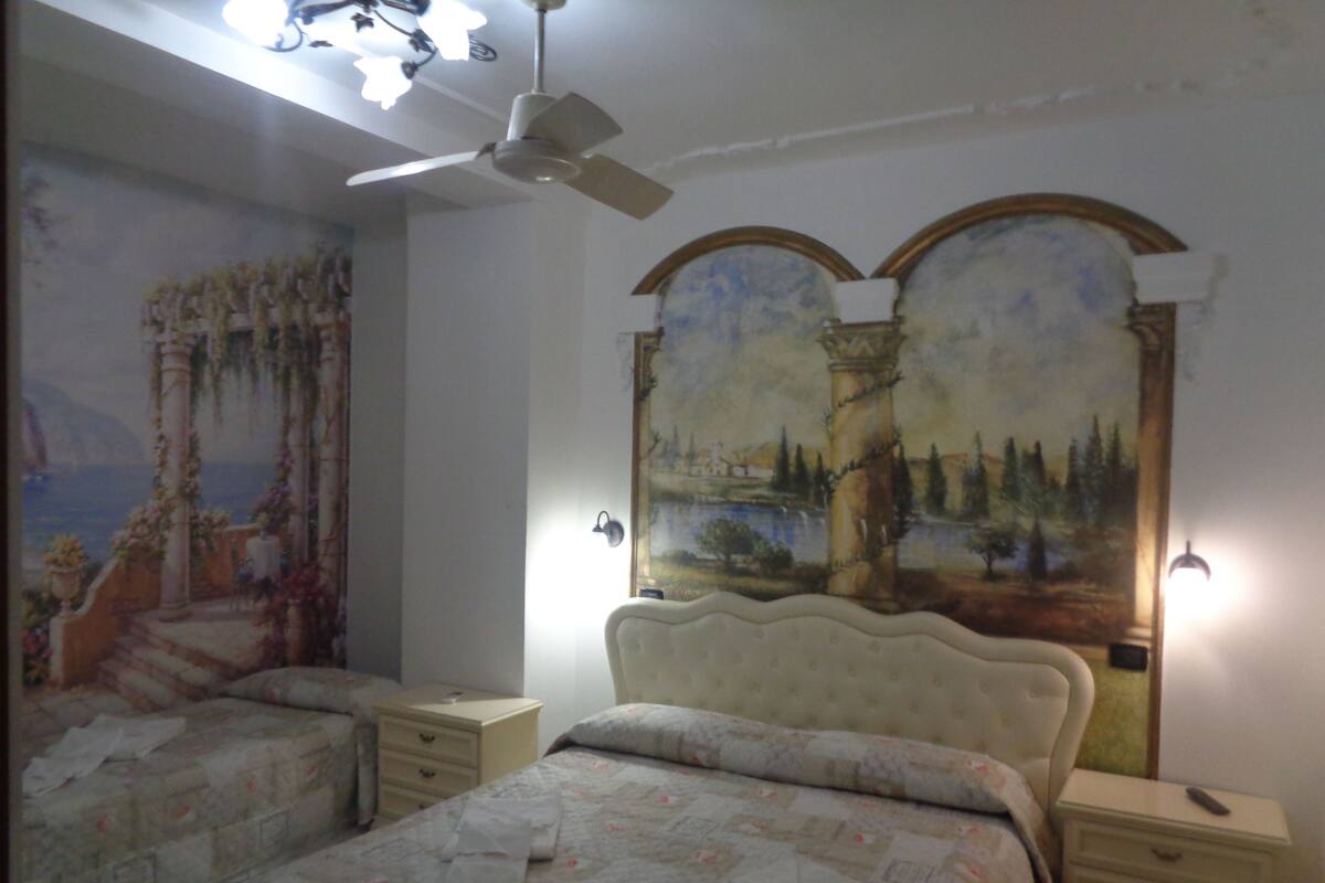Ein Schlafzimmer mit zwei Betten, einem Deckenventilator und einem Wandgemälde.