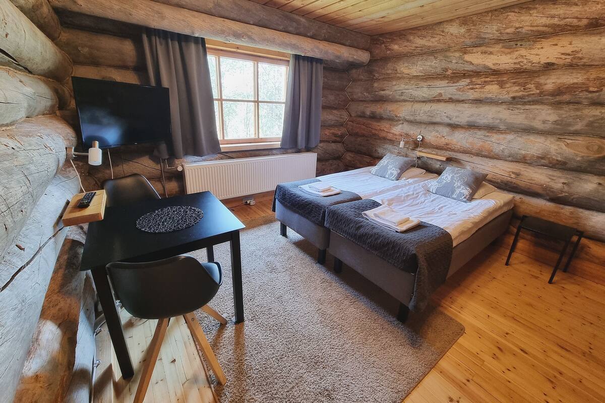 Une chambre de style rustique avec un lit, un bureau et une chaise, une télévision et une fenêtre avec des rideaux.