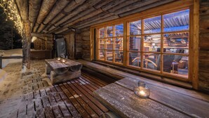 L’intérieur d’une cabane en rondins, avec une grande fenêtre, des bancs en bois et une table sur laquelle est posée une bougie.