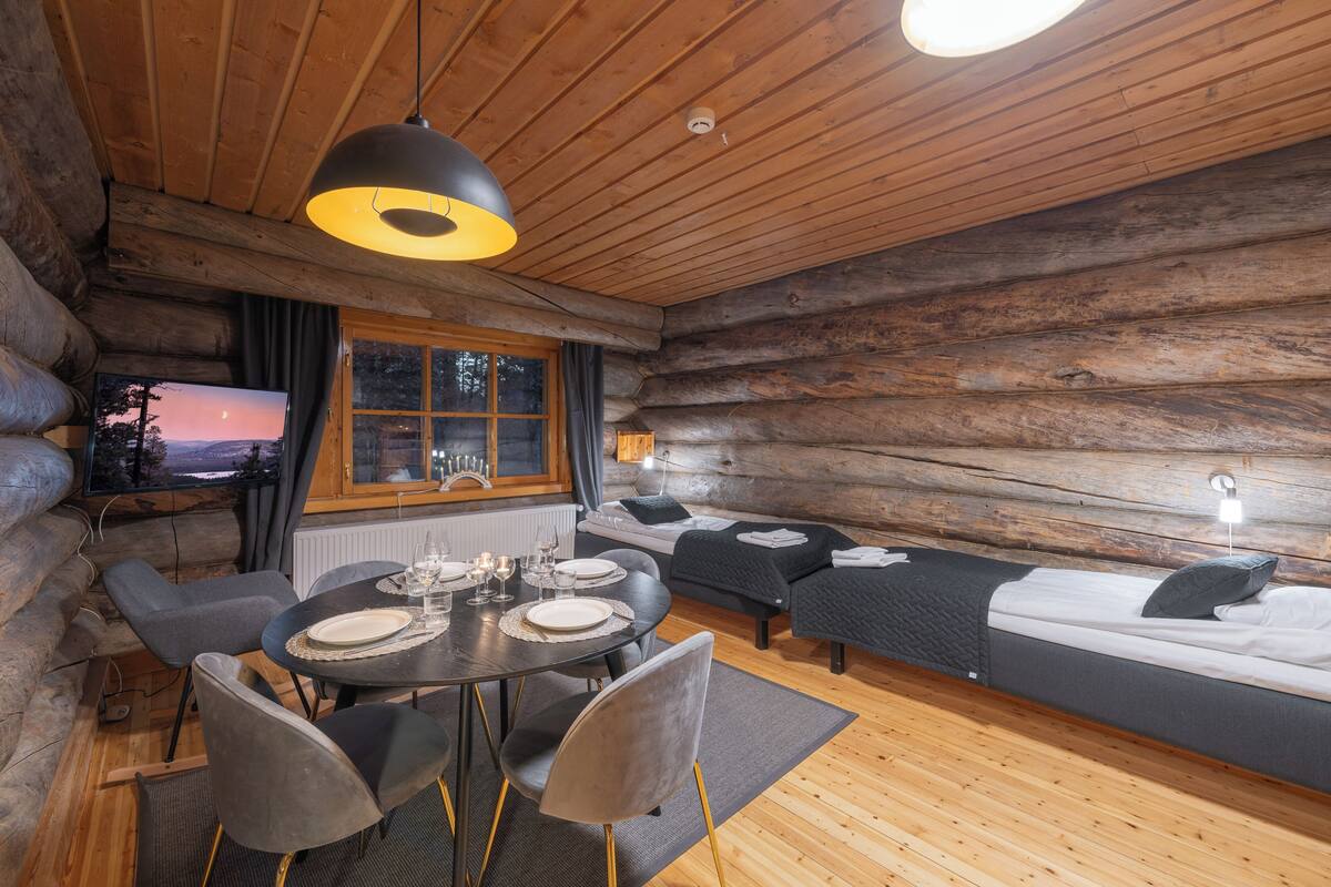 L’intérieur d’une cabane en rondins comprend un coin repas, un canapé-lit et un téléviseur qui diffuse une vue sur le coucher du soleil.