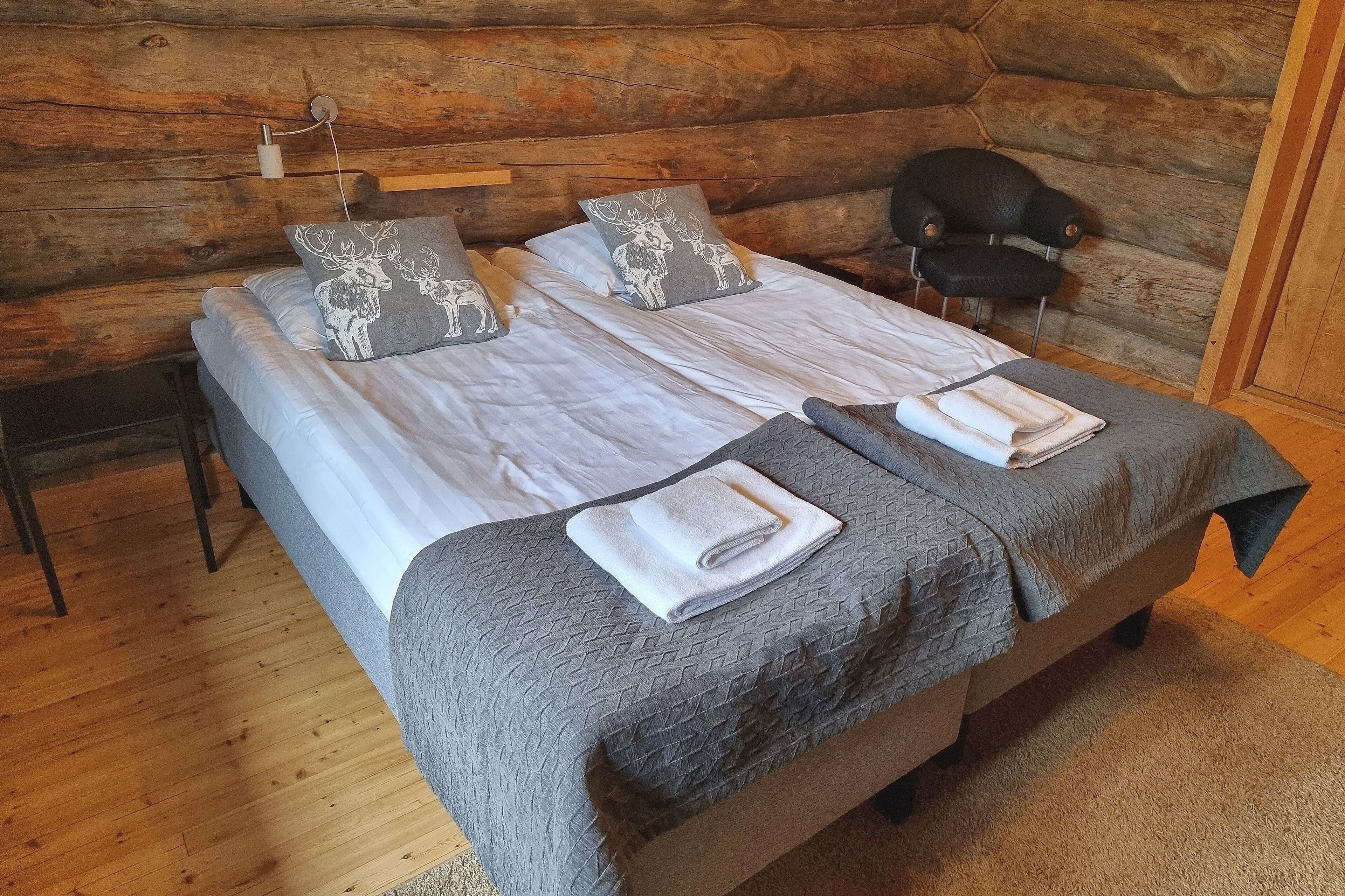 Una cama doble con dos almohadas, una silla y una mesita en una habitación de cabaña de troncos.