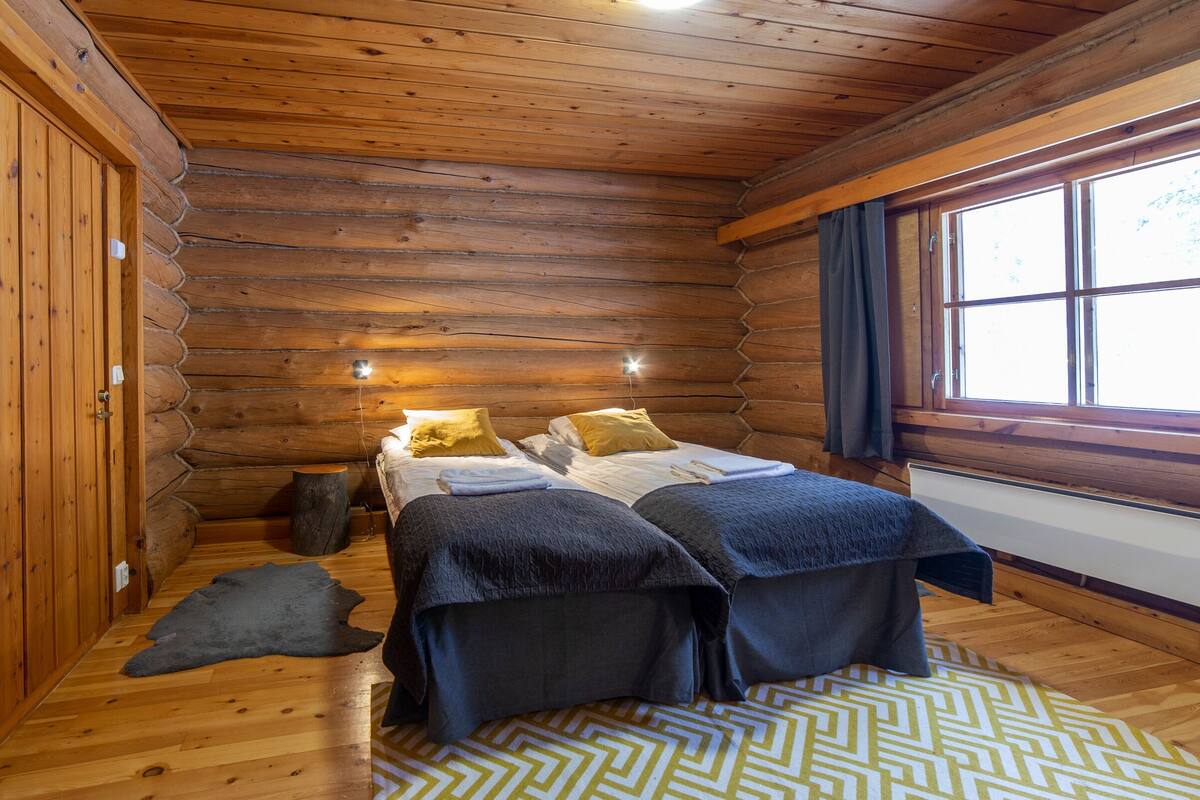 Une chambre à coucher située dans une cabane en rondins, avec un lit, deux oreillers, un tapis et une fenêtre avec des rideaux.