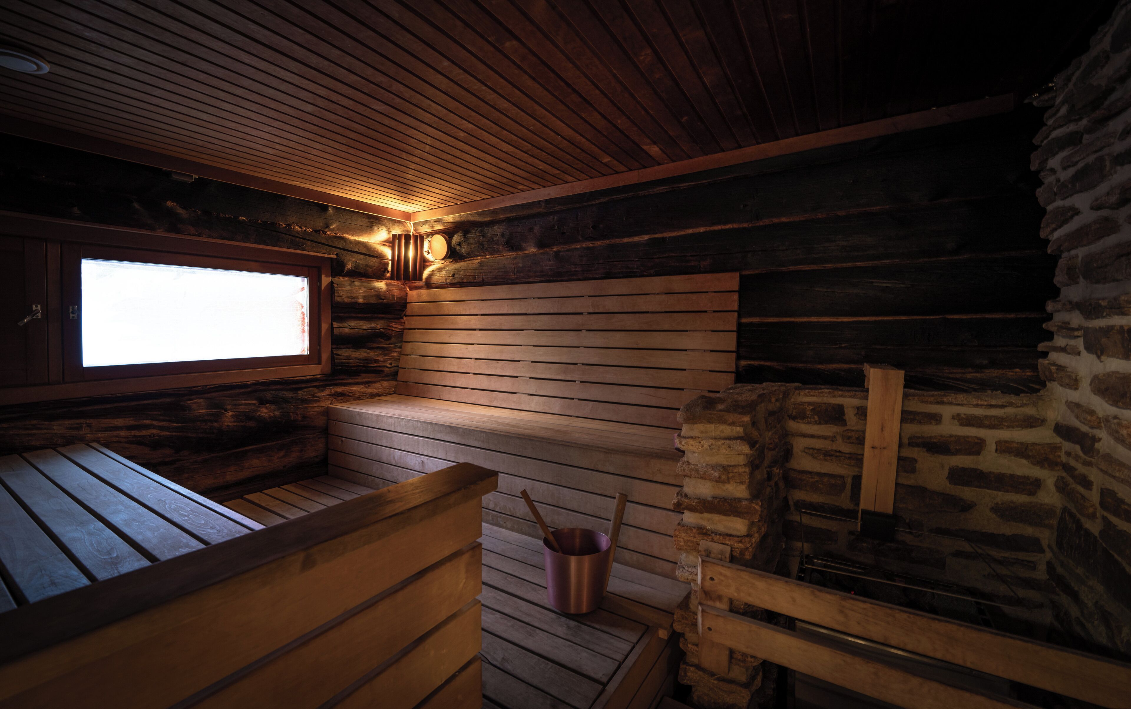 Un sauna avec des bancs en bois, un mur en pierre et une fenêtre.