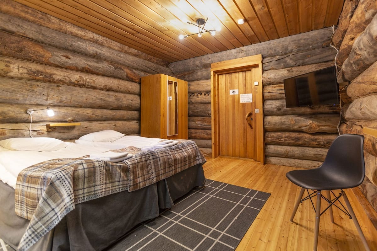 Une chambre aménagée dans un chalet en rondins, avec un lit, une chaise, une armoire en bois et une porte.