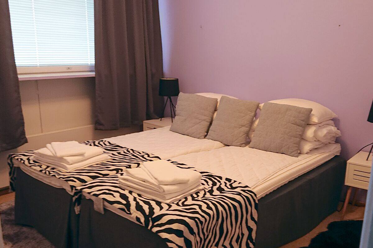 A neatly made bed with a zebra-patterned blanket, a bedside lamp, and a window with curtains.