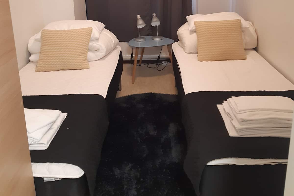 A small, compact room with two single beds, a small table with two lamps, and a black furry rug.