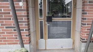 A brick building entrance with a glass door, a potted plant, and a metal grate. -  Kuukkeli Apartments Sodankylä (Sodankyla)