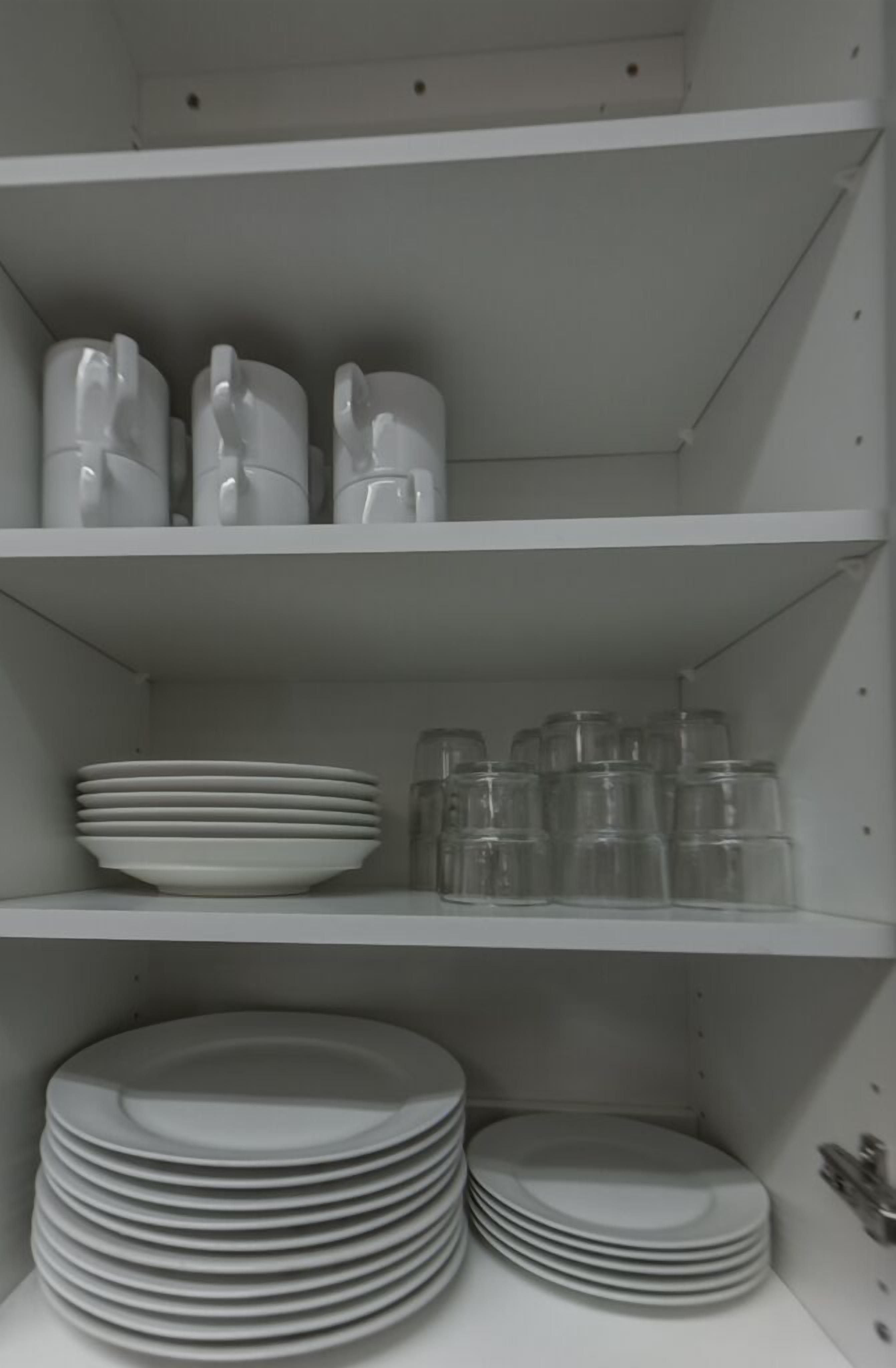 A white shelf with stacked plates and clear glass containers.