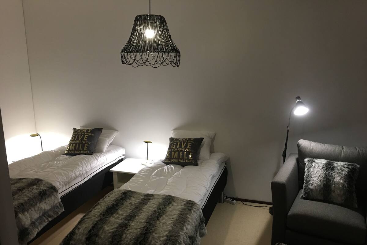 A small, well-lit room with two single beds, a chair, and a table.