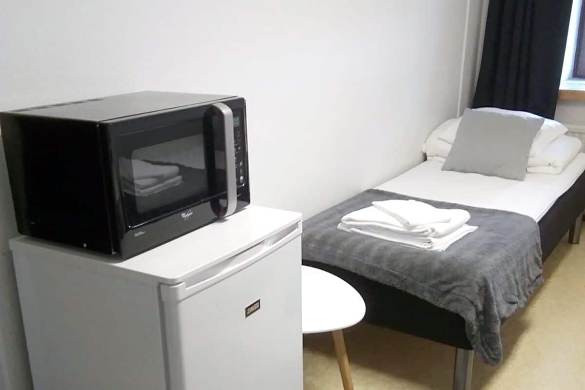 A compact hotel room with a bed, a small bedside table, a microwave, and a refrigerator.