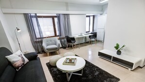 A modern living room with a black sofa, a round coffee table, and a grey armchair. There is a desk with two chairs and a potted plant. -  Kuukkeli Apartments Sodankylä (Sodankyla)