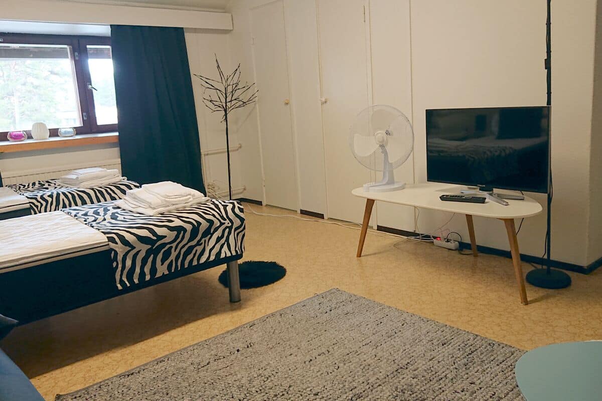 A hotel room with a bed, a TV, a desk, and a window with curtains.