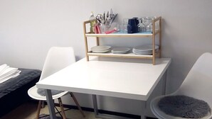 A small dining area with a white table, two chairs, and a shelf with plates and cutlery. -  Kuukkeli Apartments Sodankylä (Sodankyla)