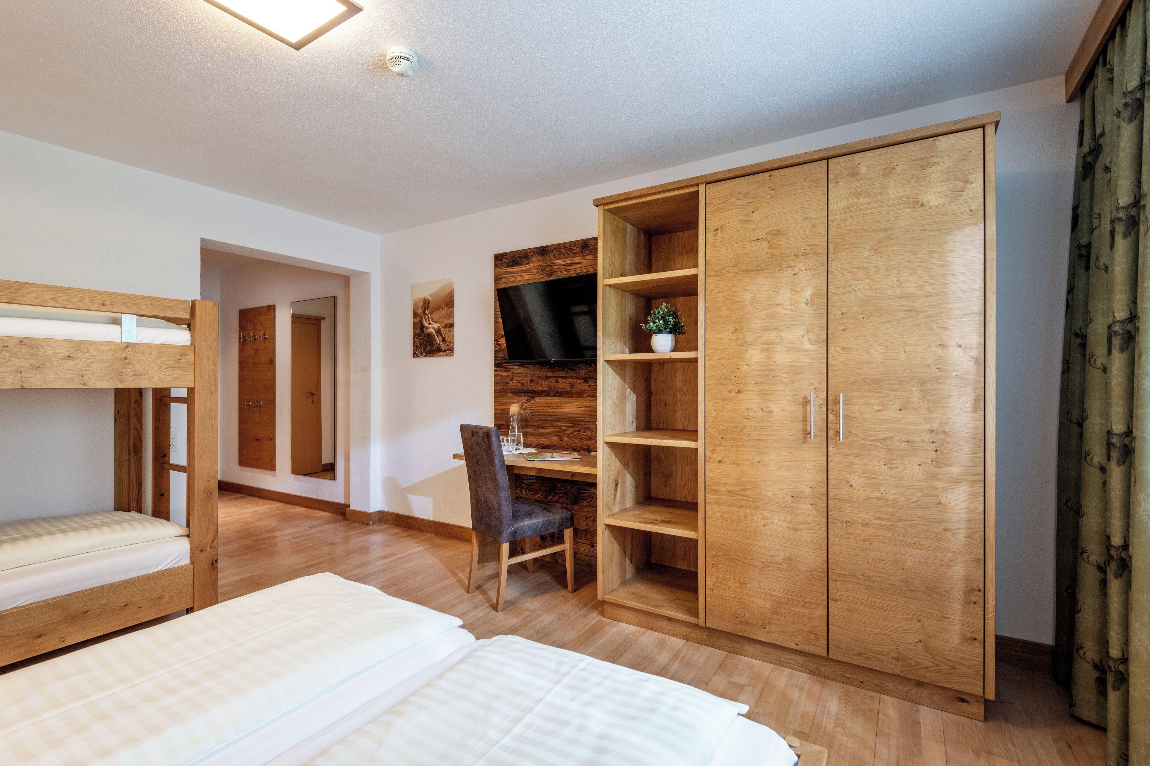 A bedroom with bunk beds, a wooden wardrobe, a desk, and a chair.