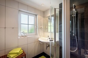 Ein modernes Badezimmer mit einer behindertzugänglichen Glasdusche, einem weißen Waschbecken und einem Fenster mit Blick.