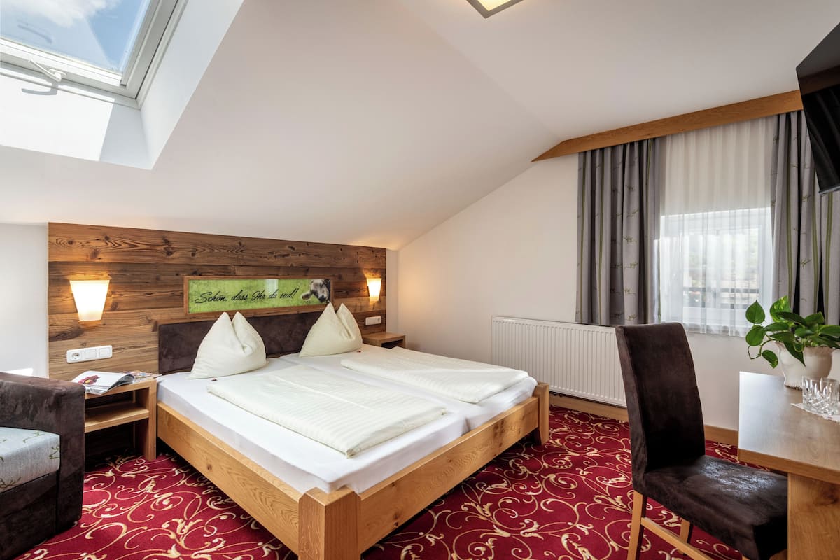Habitación de hotel con una cama de madera, un escritorio, una silla, una ventana con cortinas y una planta.